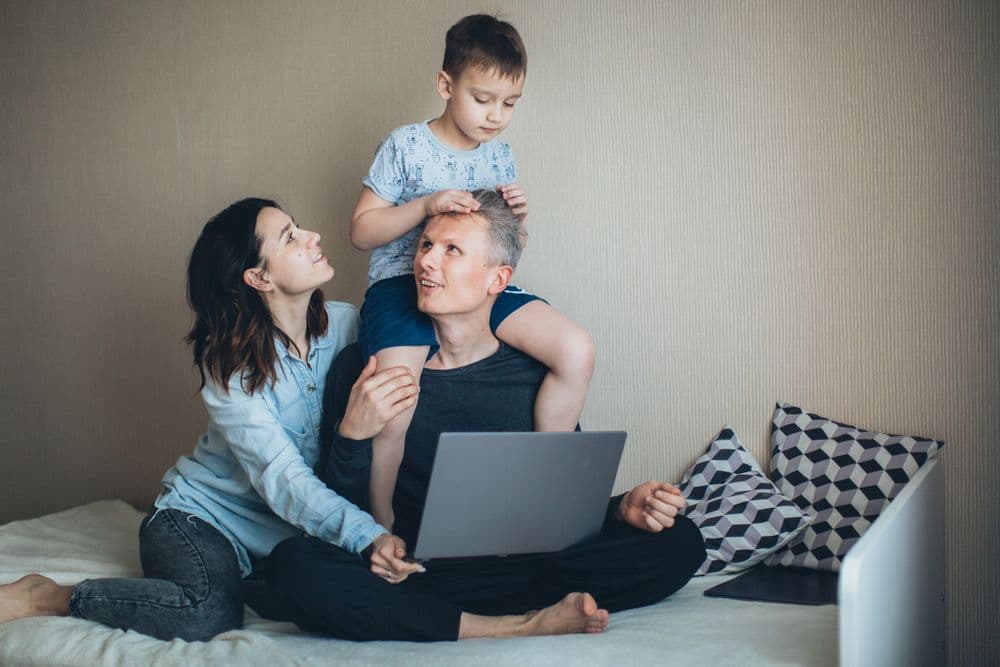 Famille souriante à la maison, ordinateur portable ouvert sur les genoux